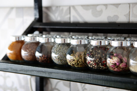 Glass jars with different types of spices on a shelf. Colorful photo of traditional spices. Pepper, cardamom, curry, turmeric, clove, lavender, seeds in small jars. Healthy eating concept. 