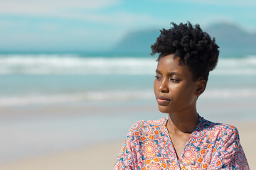 Thoughtful african american young woman with short curly hair looking away against sea on sunny day