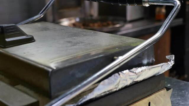 the hand of the cook put two rolls of doner kebab in pita bread into the heated grill for frying. The stage of cooking shawarma, roasting in the grill. Fast food restaurant