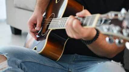 Close up view of man that playing acoustic guitar indoors when sitting on the floor