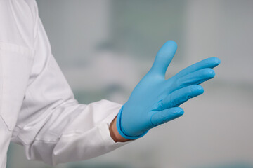 Close-up of hands putting on medical gloves in front of a clinic/ICU room 