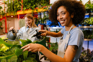 Two multinational florist girls watering potted plants in flower shop