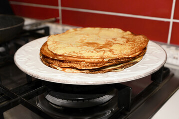 Plate of freshly made crepes on stove in kitchen, closeup