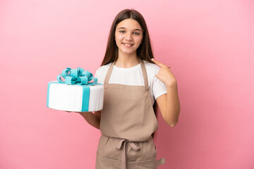 Little girl with a big cake over isolated pink background giving a thumbs up gesture
