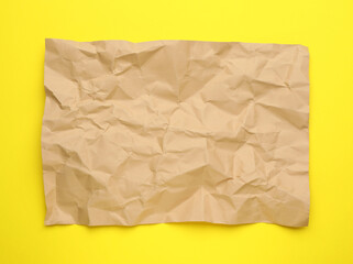 Sheet of crumpled brown paper on yellow background, top view