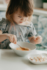 a little girl is sitting at the kitchen table eating soup