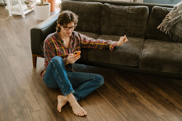 White man in glasses using mobile phone while sitting on floor