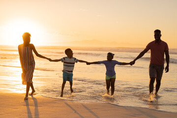 African american young parents holding son and daughter's hands while standing at shore against sky