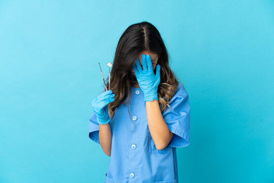 Woman dentist holding tools over isolated on blue background with tired and sick expression