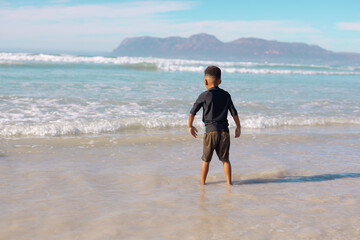 Rear view of african american boy standing in sea against sky during sunny day