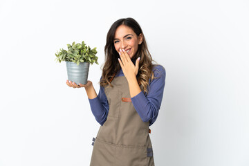 Gardener girl holding a plant isolated on white background happy and smiling covering mouth with...