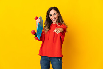 Young caucasian woman isolated on yellow background with a skate and pointing to the front