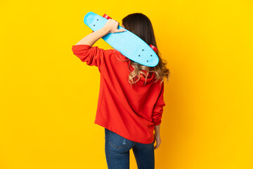 Young caucasian woman isolated on yellow background with a skate in back position