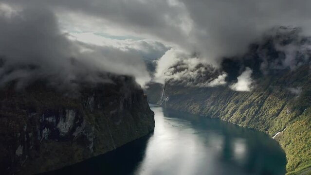 Aerial view of the Geiranger fjord. Ethereal clouds whirl in the sky. Pan forward.