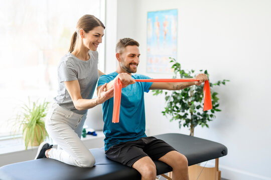 Modern rehabilitation physiotherapy woman worker with man client using red elastic