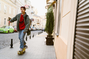 Asian boy listening music while skateboarding at street