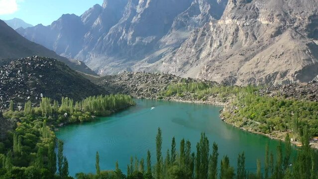 aerial drone of a boat at Upper Kachura Lake in Skardu Pakistan on a sunny summer day surrounded by green forest and unique mountain range in the distance.