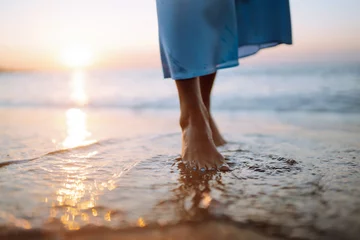 Zelfklevend Fotobehang Close up van blote voeten van een vrouw wandelen op een strand bij zonsondergang. Zomer tijd. Reizen, weekend, ontspannen en lifestyle concept. © maxbelchenko