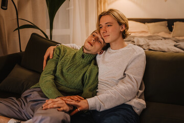 Obraz premium Young gay couple hugging and resting on couch while watching tv