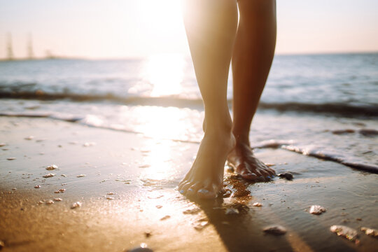 Close up of a female's bare feet walking at a beach at sunset. Summer time. Travel, weekend, relax and lifestyle concept.