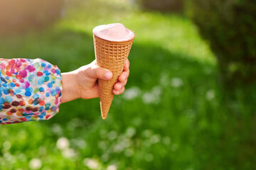 Close-up hand with ice cream in a waffle cone against the background of a summer green lawn. Vacation and summer time concept