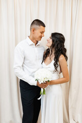 Smiling wedding couple posing in front of a white curtain.