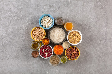 Obraz na płótnie Canvas Concept of vegetarian food and diet on gray concrete background, legumes, seeds and cereals in colored bowls grouped with copy space
