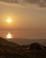 Fototapeta na wymiar A tent wild camping in glorious sunset coastal mountain location of Snowdonia UK