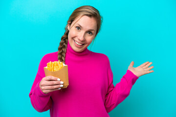 Young caucasian woman holding fried chips isolated on blue background extending hands to the side for inviting to come