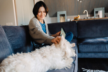 White mature woman using laptop while petting her dog on couch