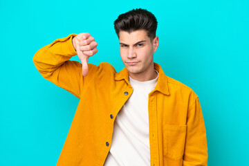 Young handsome caucasian man isolated on blue bakcground showing thumb down with negative expression
