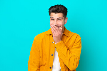 Young handsome caucasian man isolated on blue bakcground happy and smiling covering mouth with hand
