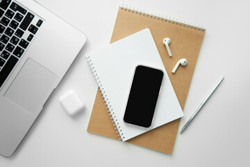 Mobile phone with blank black screen on desktop. Business concept template: laptop, mobile phone, wireless headphones, notepad and pen.