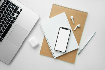 Mobile phone with blank white screen on desktop. Business concept template: laptop, mobile phone, wireless headphones, notepad and pen.