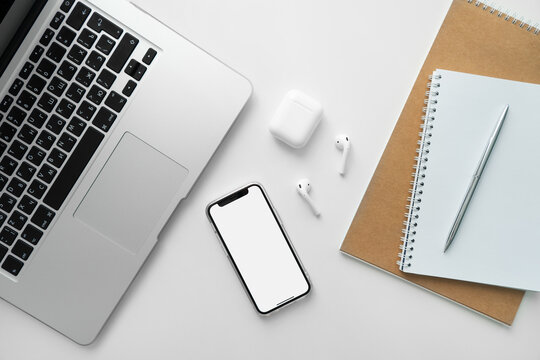 Mobile phone with blank white screen on desktop. Business concept template: laptop, mobile phone, wireless headphones, notepad and pen.