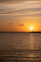 Sunset over Mykonos island, Cyclades, Greece. Lighthouse, orange yellow sky sparkle sea. Vertical