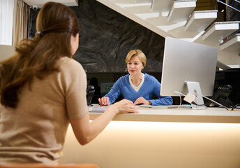Attractive pleasant woman, experienced consultant receptionist consulting a female client at...