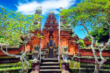 Beautiful red hindu temple gate, green trees, blue sky, mythological figures - Pura Batuan, Ubud,...