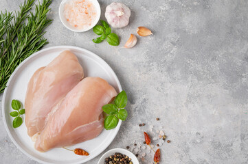 Raw chicken breast or fillet with salt, pepper and fresh herbs on a white plate on a gray...