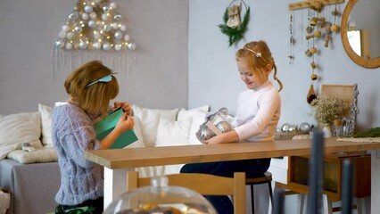 Two cute little girls exchange gifts with each other cosy room background. Concept: children's congratulations. Two loving sisters