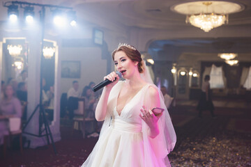 Beautiful bride in a wedding dress holds a microphone and sings at a banquet. A surprise for the...