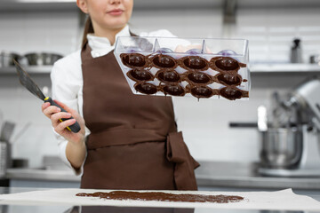 Chef or chocolatier makes sweet chocolates in a professional kitchen. She turns the mold over and...
