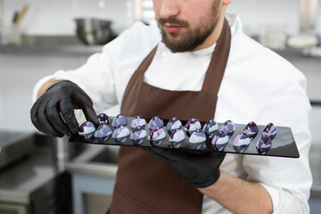 Close-up of the hand of a male pastry chef-a man laying out colored chocolates on a black mirror...