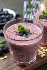 Glass of tasty blueberry smoothie with oatmeal on wooden board, closeup
