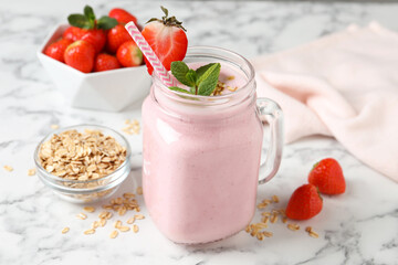 Mason jar of tasty strawberry smoothie with oatmeal and mint on white marble table