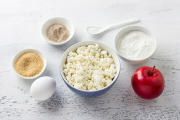 Ingredients for making syrniki with apple: cottage cheese, egg, apple, rice flour, sugar, vanilla sugar, salt on light gray background. Cooking delicious gluten free homemade food