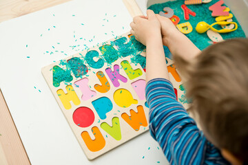 kid learning to read alphabet through game. Sensory activity with colored rice and wooden letters. Educations at home, pre-school education, Montessori methodology