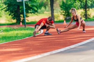 Attractive young couple stretching together on a race track after exercising outdoors