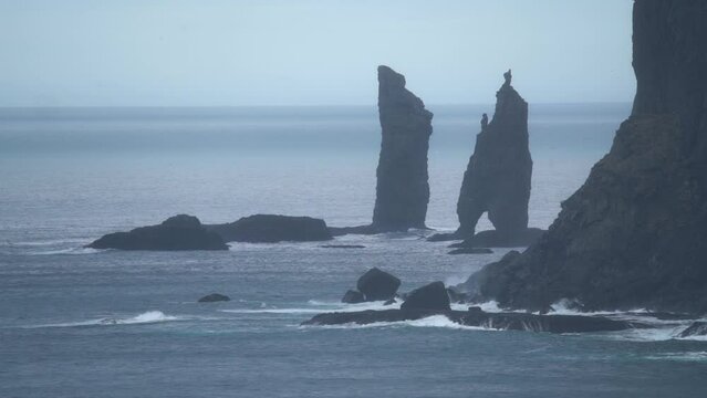 Wide shot of Risin og Kellingin sea stacks on Faroe Island with Atlantic Ocean in background - Slow motion