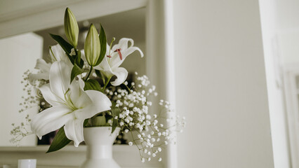 bouquet of white flowers in a bright interior. selective focus. lily and gypsophila in a white vase close-up
